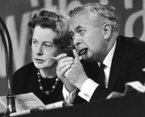 Black and white photograph of two politicians engaged in discussion at a conference, with one holding a pencil and the other looking attentively.